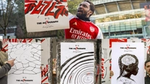 Arsenal fan in a football shirt holding The Autograph poster outside of the Emirates stadium