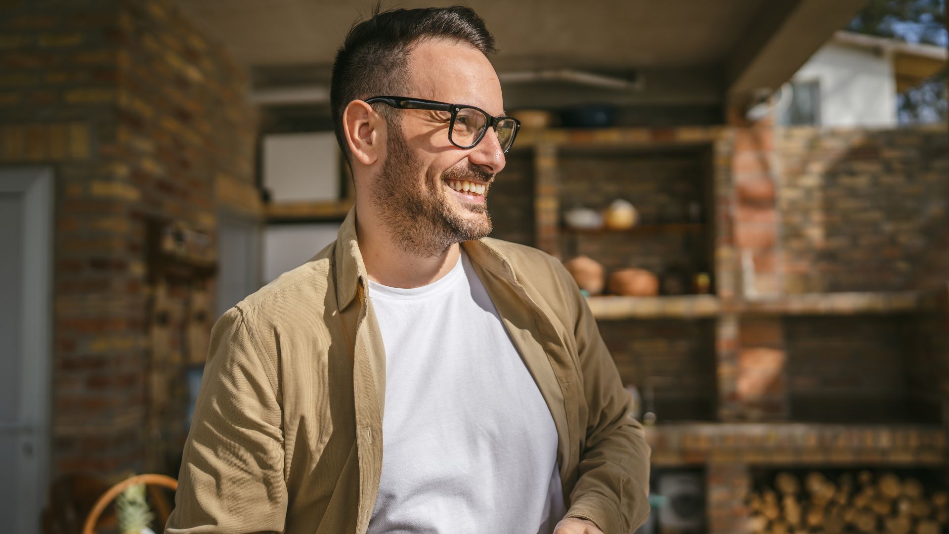 Smiling man with glasses outdoors in sunlight.