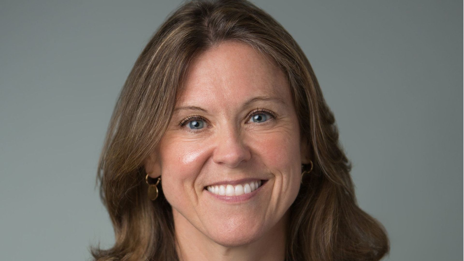 Image shows headshot of a white woman with shoulder length hair smiling at the camera.
