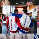 Two people walk side by side inside an Arsenal stadium concourse with their arms around each other’s shoulders, wearing red‑and‑white and blue‑and‑white jackets with ‘VARZENAL’ printed vertically on the back, with the Arsenal crest visible ahead and fans in the background