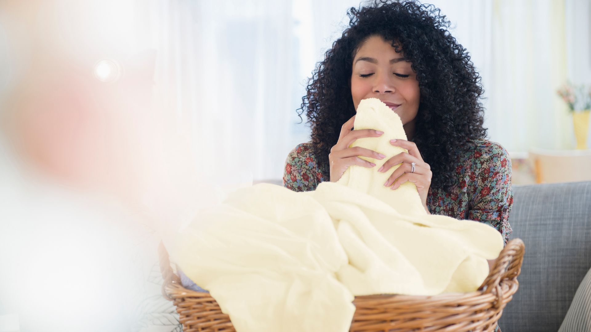 A person pulling a blanket from a basket close to their nose and smelling it.