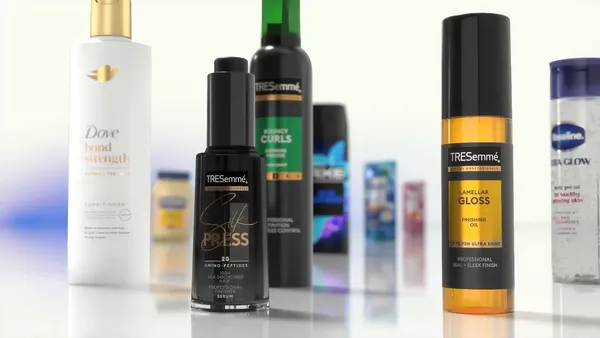 A close-up display of various hair and skincare products arranged on a reflective surface, including Dove Bond Strength conditioner, TRESemmé Silk Press serum, TRESemmé Lamellar Gloss finishing oil, and other branded items in the background.