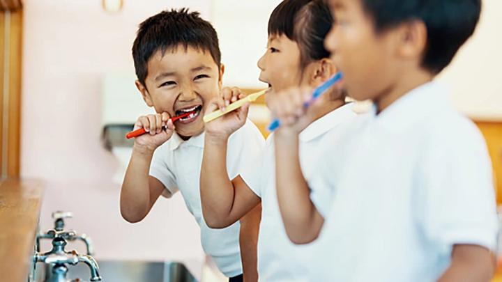 Three smiling children brushing teeth