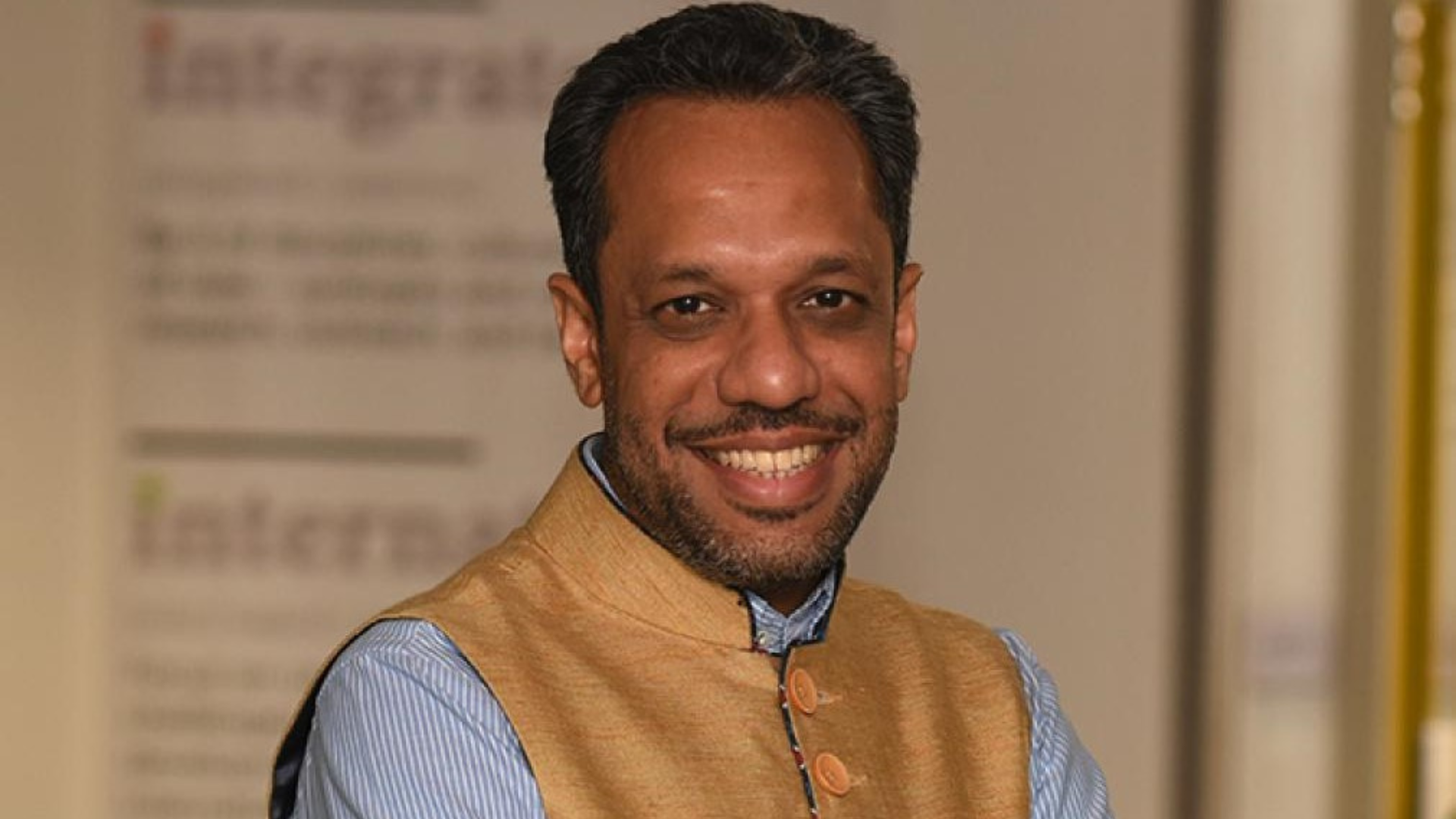 A headshot of Arunabha Gosh. Arunabha has black hair and brown eyes, and is wearing a light blue shirt and buttoned-up golden waistcoat. He is smiling at the camera.