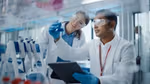 Male scientist and female scientist consider a flask of blue chemicals in a lab testing environment.