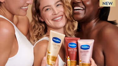 Three women laugh together whilst holding Vaseline products