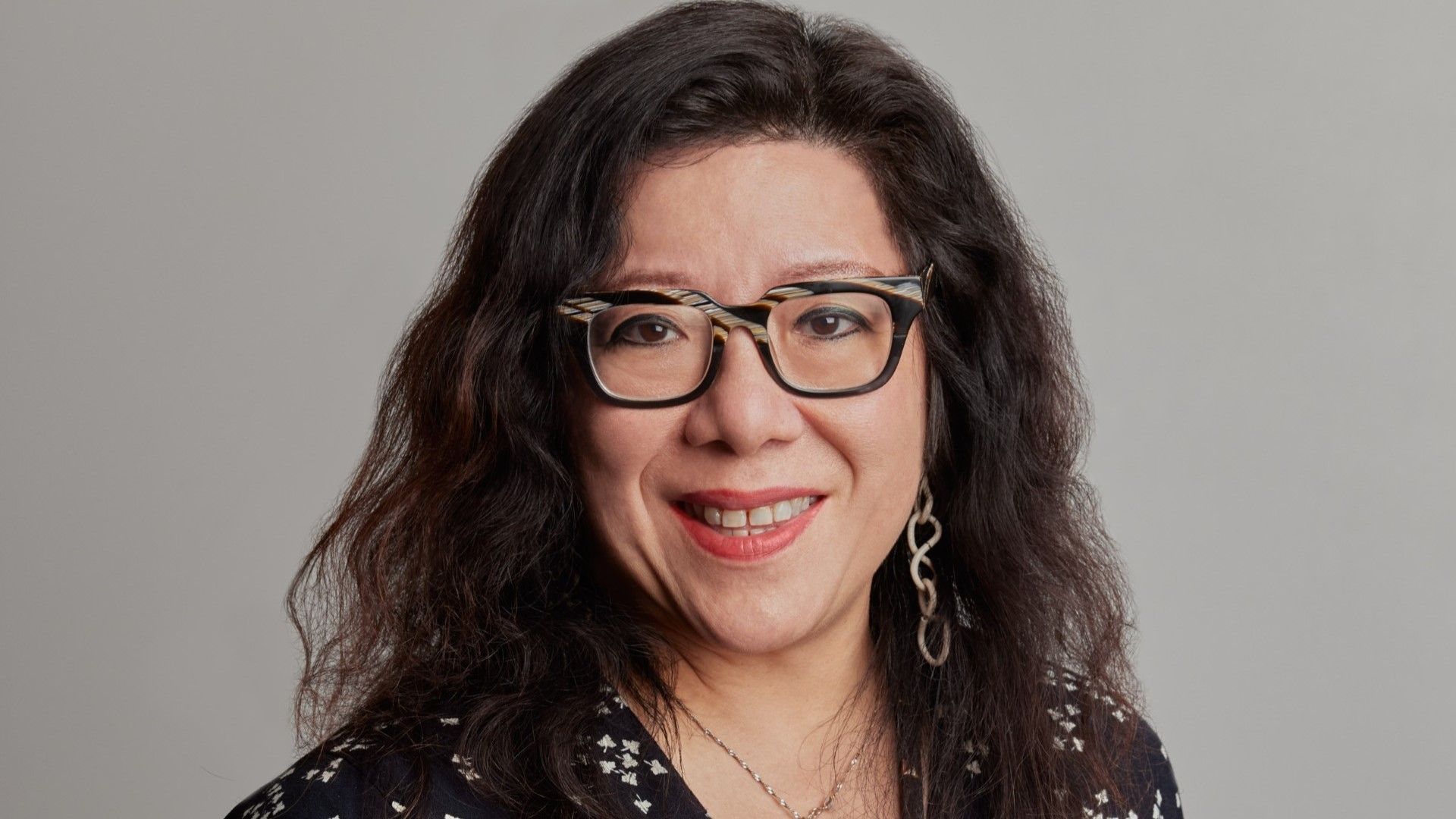 A headshot of Bernice Lee. Bernice has long brown wavy hair, and is wearing glasses and a plain black top. She is smiling at the camera.