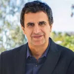 A headshot of Fernando Fernandez, Unilever CEO. Wearing a dark shirt and suit jacket with trees and bushes in the background
