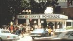 A shop displaying the name ‘Ben & Jerry’s Homemade’ with a long queue of people and several cars parked outside