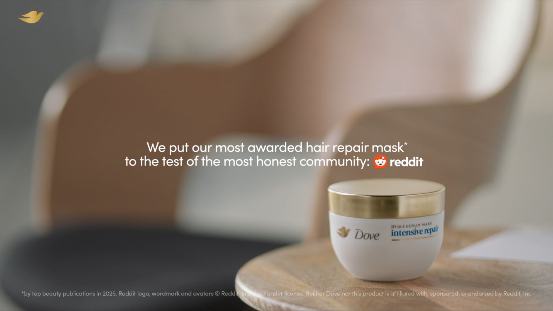 A jar of Dove Intensive Repair hair mask sits on a wooden surface in a softly lit, minimalist room with a neutral-toned chair in the background. White text on the image reads: “We put our most awarded hair repair mask to the test of the most honest community: Reddit,” with the Reddit logo displayed next to the text. A small Dove logo appears in the top left corner.