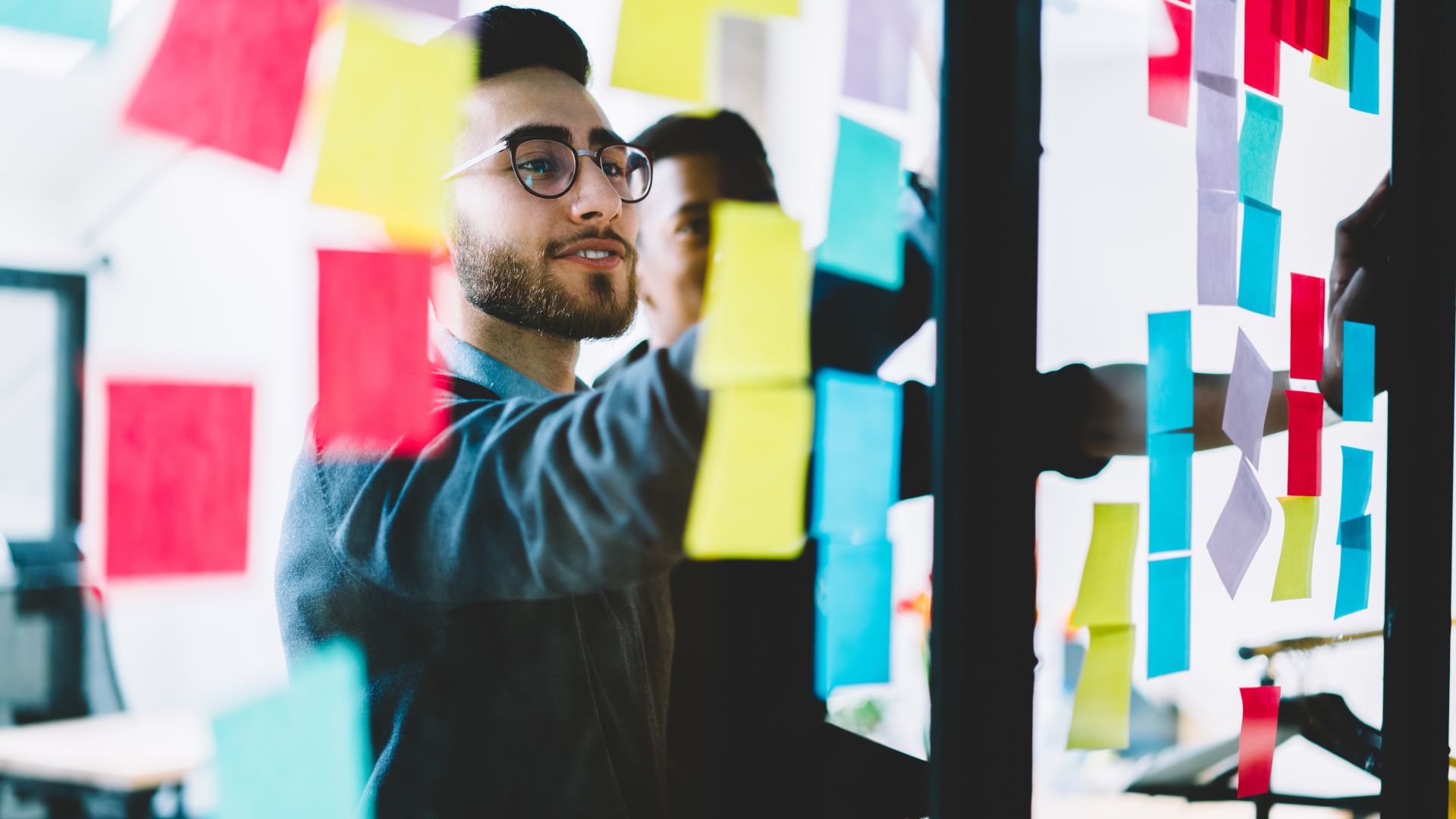 Young people learning from colourful stickers glued on glass wall during collaborative process in office