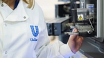 A close-up photo of a scientist wearing a white lab coat with a Unilever logo on the chest.