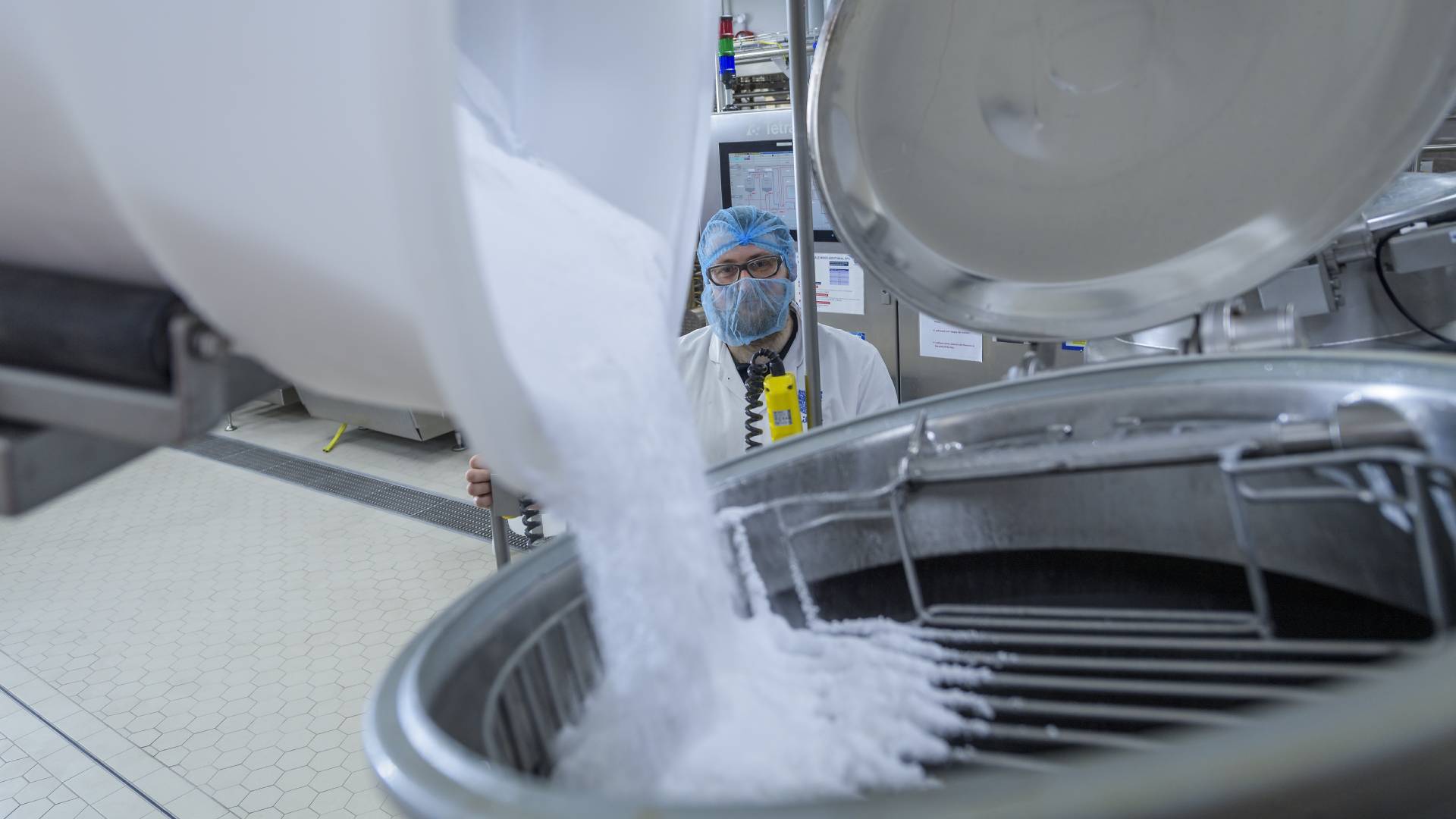R&D team member in hairnet and white coat overseeing sugar automatically poured into a mixing machine.
