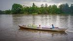 A man and a boy in a long boat on a river.