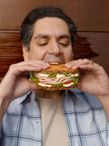 A man prepares to take a bite from a huge ham salad sandwich with mayonnaise.