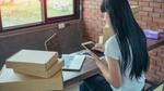 Asian woman at home online shopping. A laptop, an iPad and parcels surround her