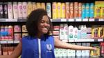 A lady, wearing a blue Unilever shirt, in a shopping aisle leaning against rows of products.