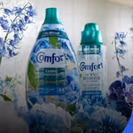 Comfort fabric conditioner and scent booster bottles surrounded by blue flowers, presented in a fresh, bright setting.