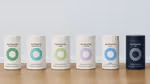 Six Nutrafol products positioned in a row on a wooden table – five are in white packaging and one appears in black.