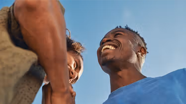 Two men smiling and shaking hands while coming in for a hug.