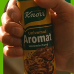 A hand grabbing a container of Knorr Universal Aromat to use as a condiment while cooking.