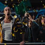 Excited football fans in a stadium cheer loudly as yellow confetti falls around them