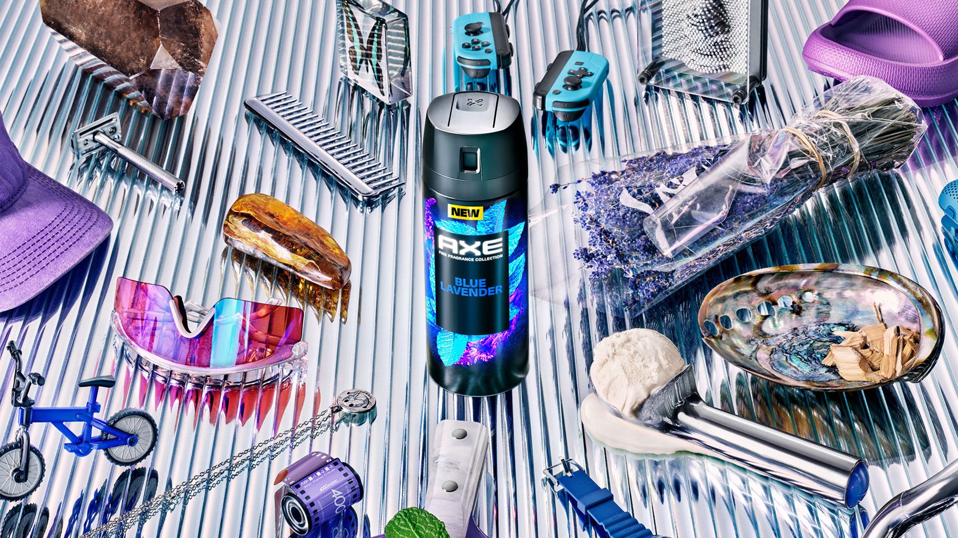 A flatlay photo with a can of Axe Blue Lavender fine fragrance deodorant spray in the centre. Also pictured are sunglasses, a Nintendo controller, a razor and a spray of lavender. 