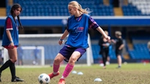 A blonde young woman playing football in a blue kit. Rexona's Breaking Limits Program in action at Chelsea.