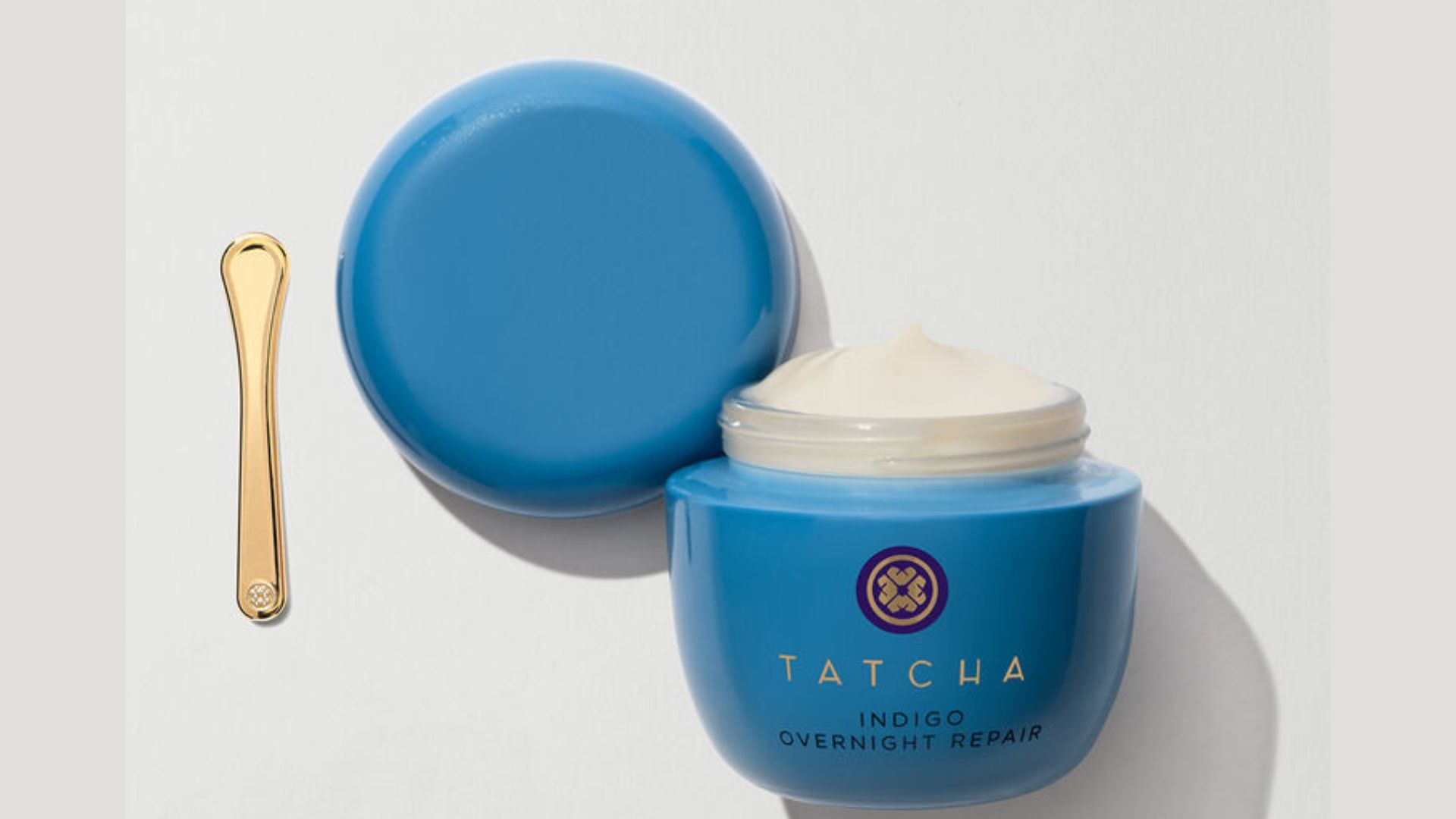 A photo of Tatcha Indigo Overnight Repair – a white rich cream in a blue glass jar with a small gold applicator.