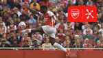 Arsenal forward Bukayo Saka, in an Arsenal kit, kicking a football in front of a crowd.