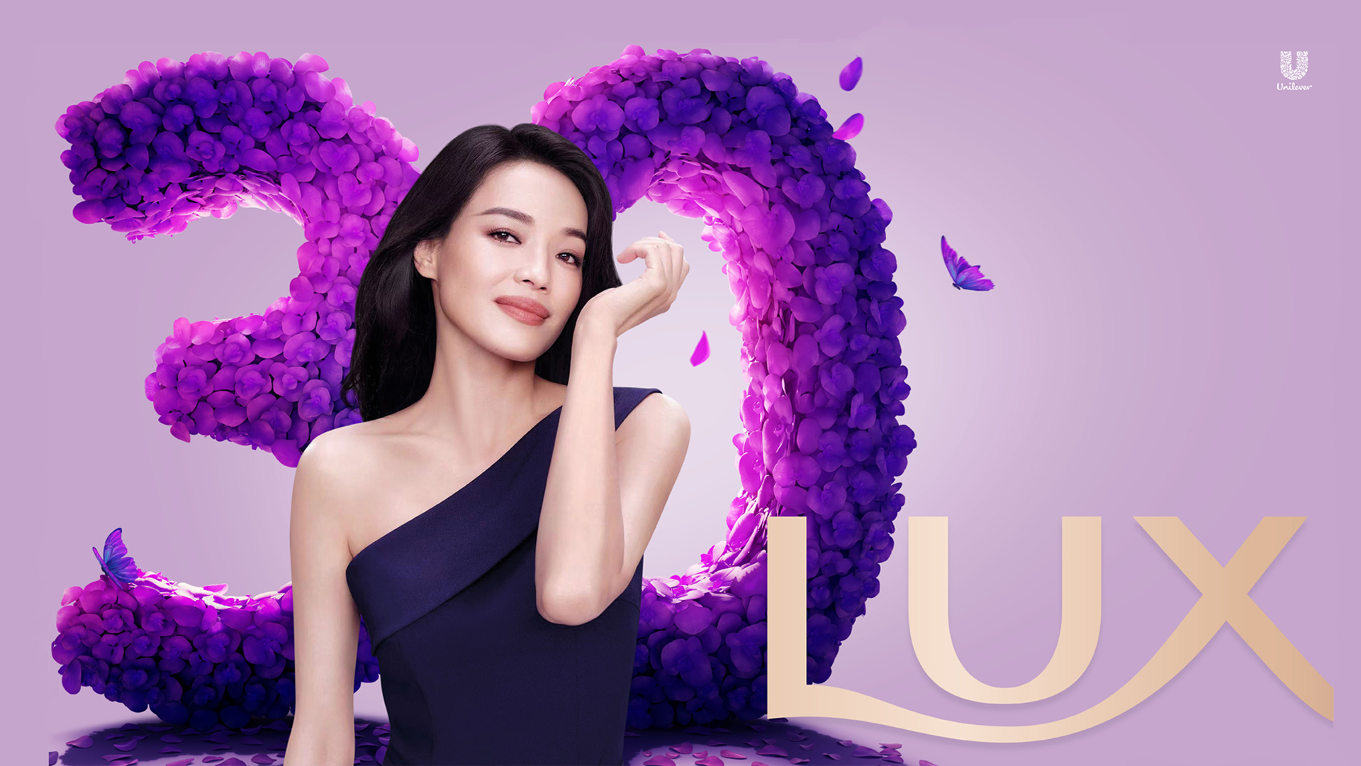 A woman in a purple dress standing in front of a large ‘30’ which is made out of petals.