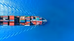 An image of a boat from above, loaded with shipping containers, sailing on open water.