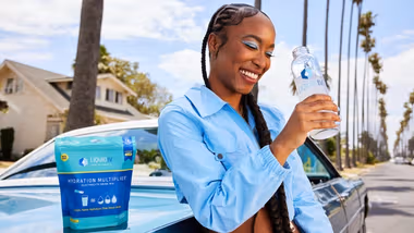 Woman standing by car drinking bottle of Liquid I.V. The product sits within Unilever’s Beauty & Wellbeing business group.