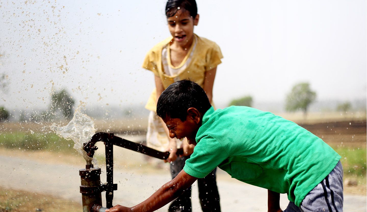 Two children playing and drinking water by an outdoor water tap