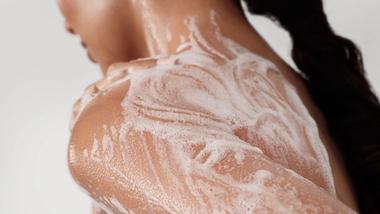 Back view of a woman with her hair in a ponytail whose naked back and shoulders are lathered with Dove’s foaming body wash