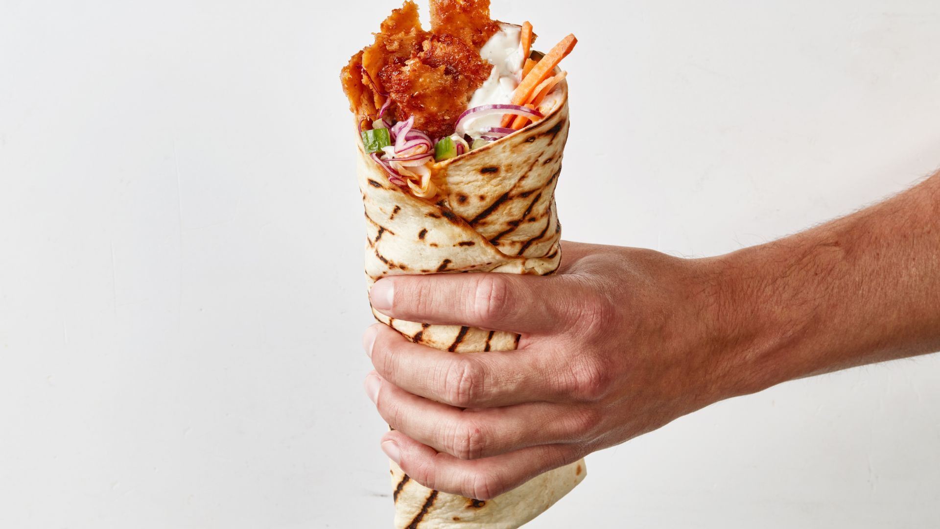 A close-up of a hand holding a plant-based döner kebab wrap