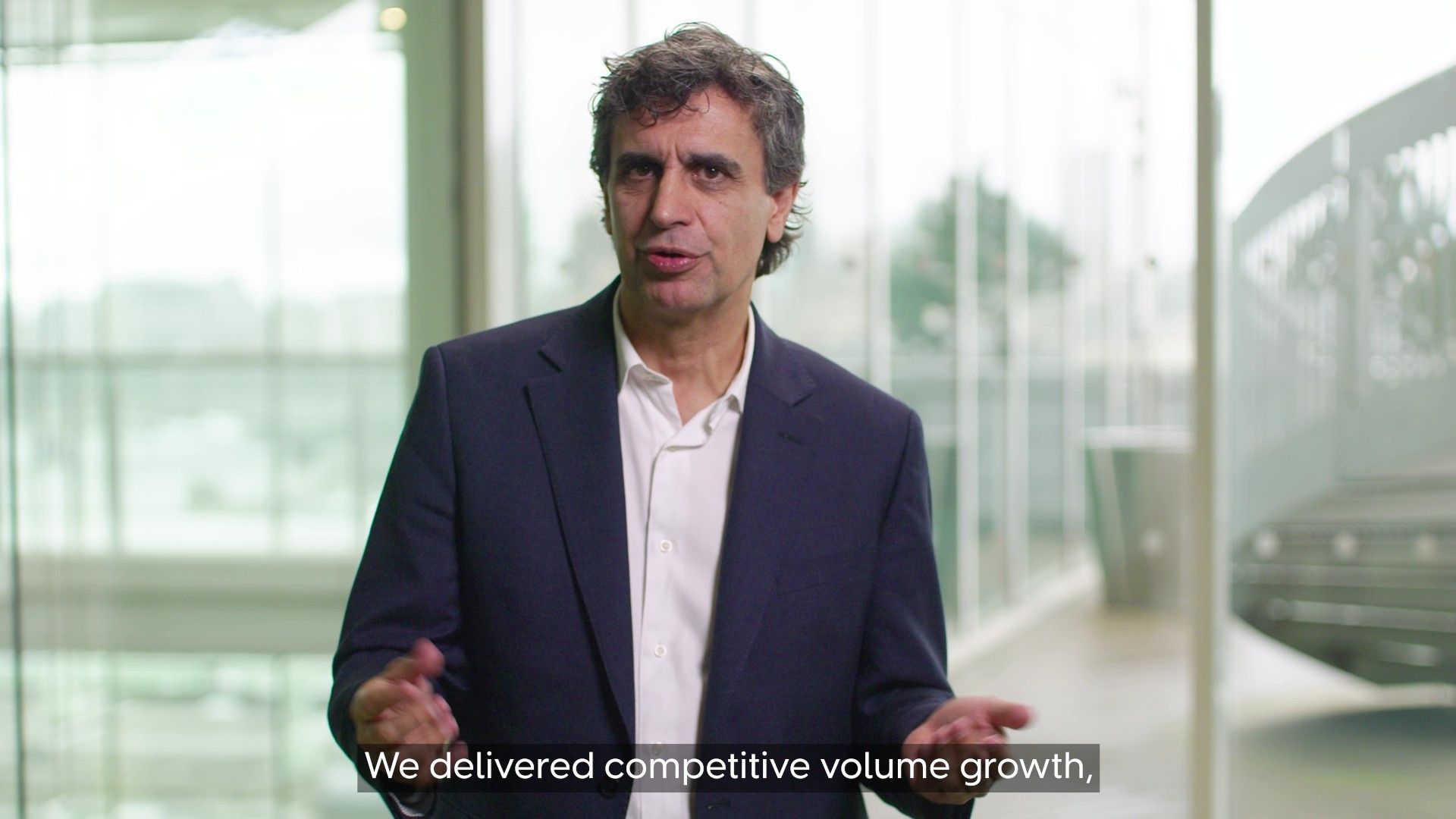 A person wearing a dark blazer and white shirt stands indoors in front of large windows. On-screen text in a blue box reads ‘Fernando Fernandez – Chief Executive Officer.