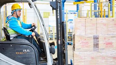 Fork lift truck driver moving a pallet of cardboard boxes labelled OMO in China