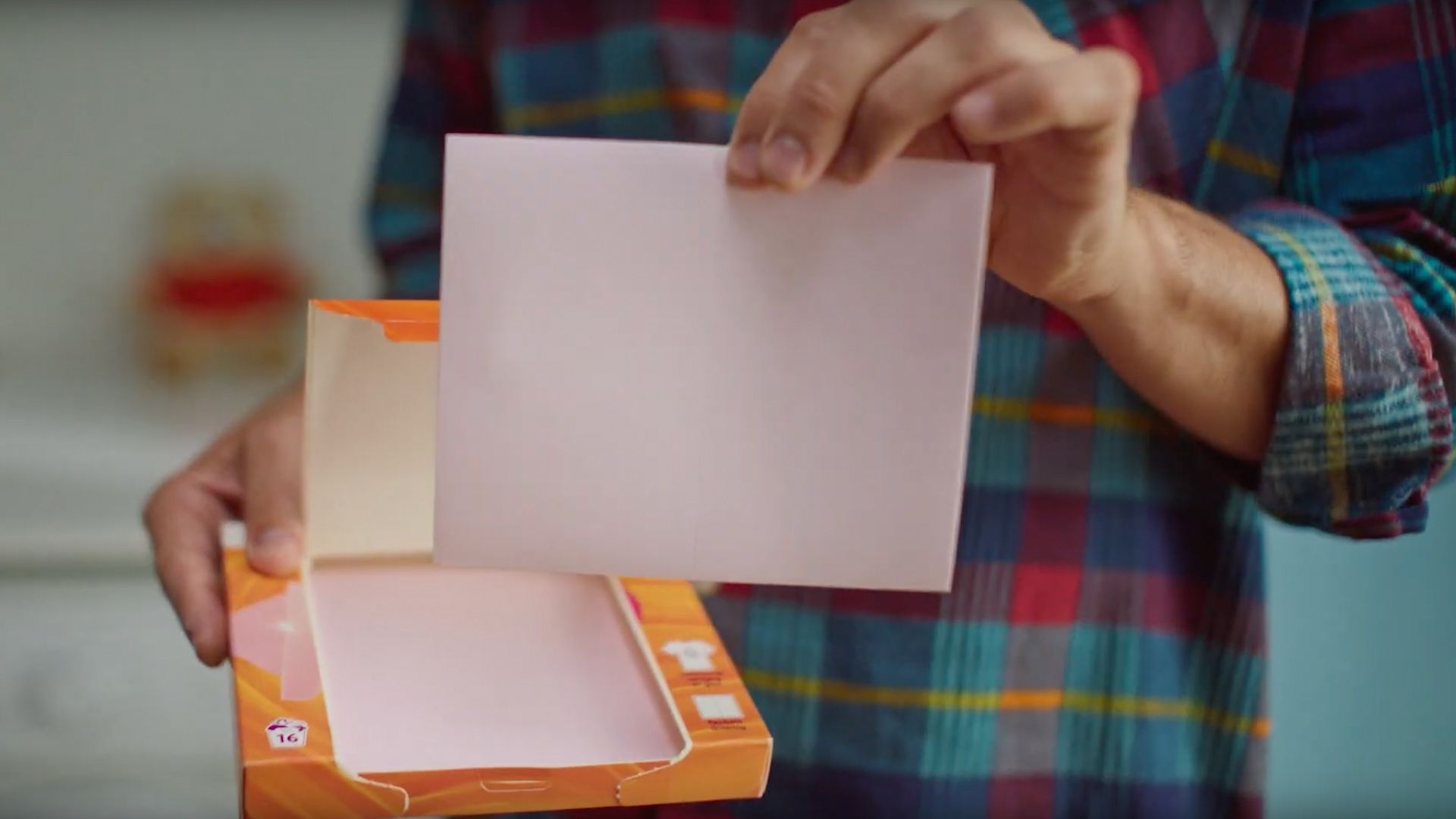 Man’s hand holding a laundry detergent sheet from Unilever’s Robijn brand.