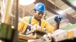 A man wearing a blue hard-hat, protective glasses and gloves working in a factory.