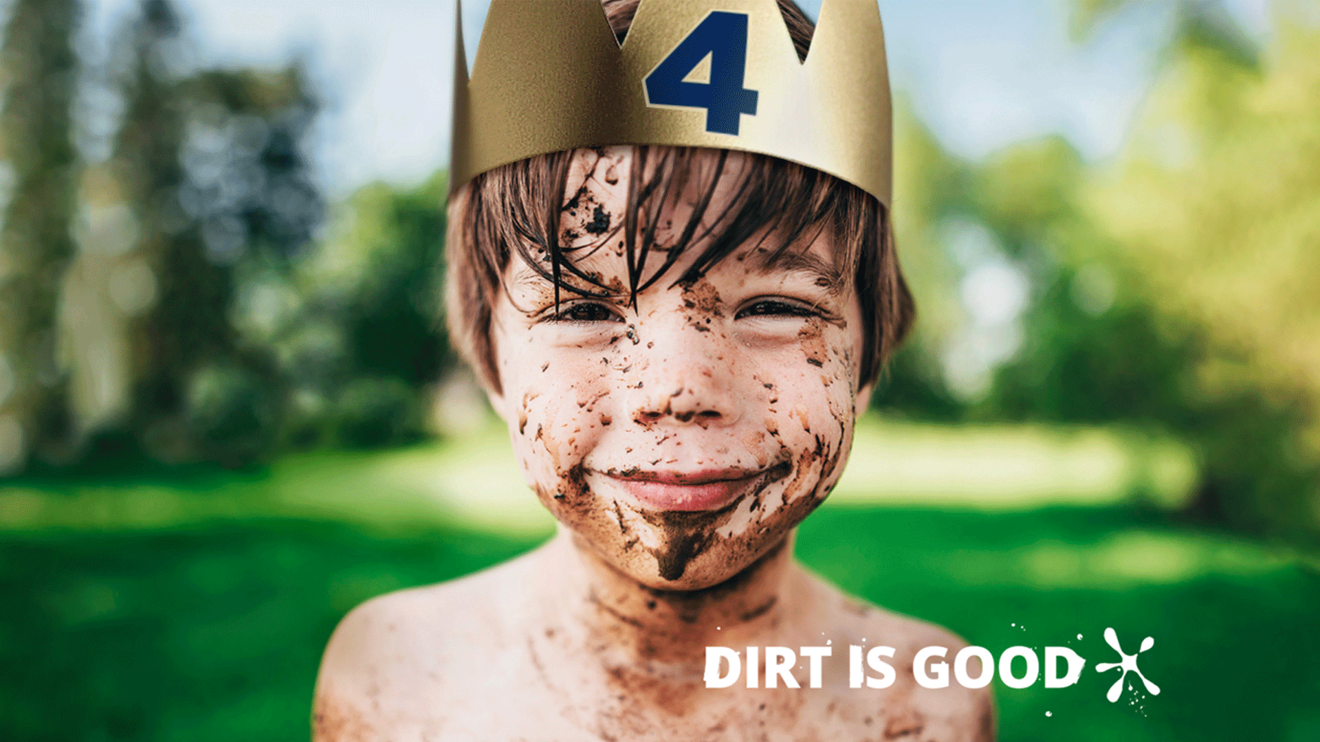 Young boy smiling, splashed in mud, wearing a gold paper crown.
