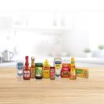 A selection of well known food and condiment brands, including Hellmann’s mayonnaise, Frank’s RedHot, Cholula Hot Sauce, Knorr seasonings, French’s mustard, and condiments, arranged side by side on a wooden table.
