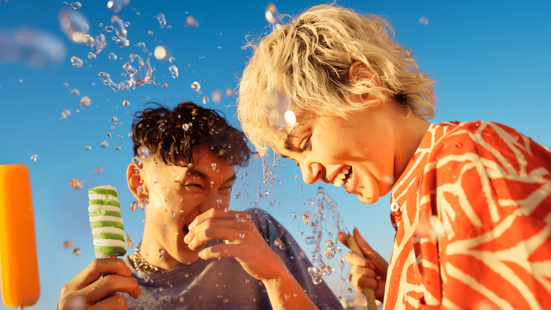Young male holding a Twister ice cream is laughing with his female companion who is spraying water and holding a Solero