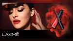 A woman with bold red lips and smokey eye make-up gazes away from the camera, holding a tube of Lakmé lip mousse.