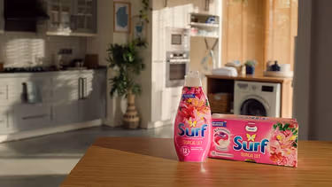 Two Surf products on a kitchen counter, with a washing machine, a row of cupboards and a plant in the background.