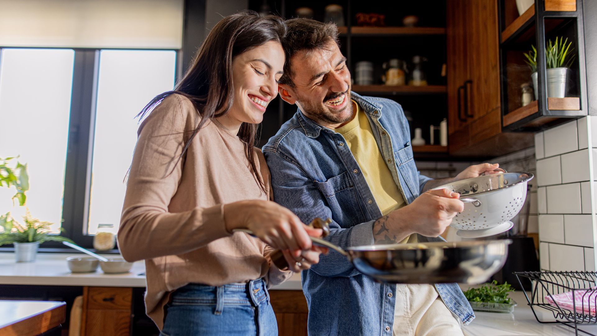 Couple smiling and cooking together in a kitchen.