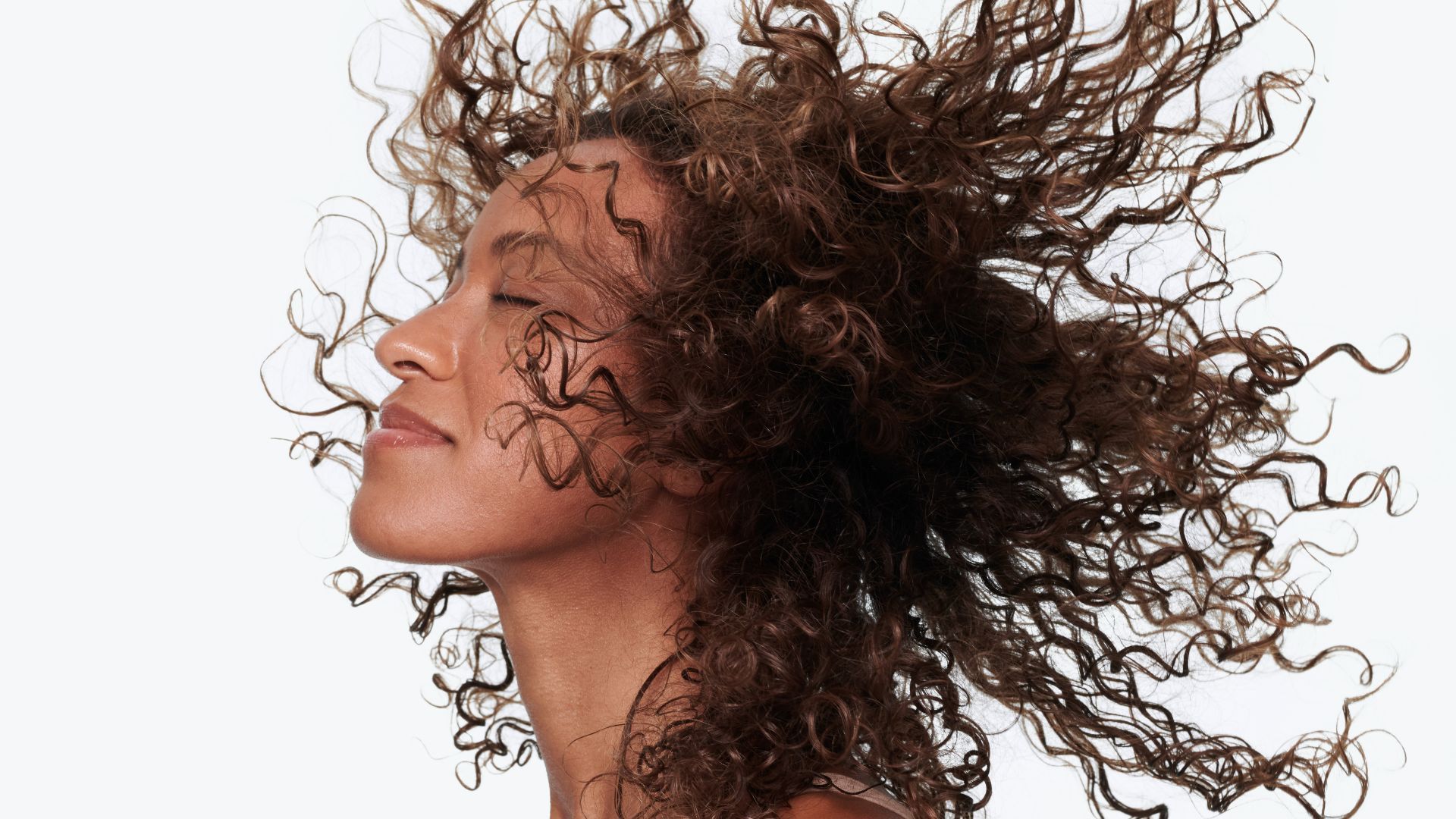 Side profile headshot of woman throwing her head back to showcase the condition of her long, mid-brown naturally curly hair