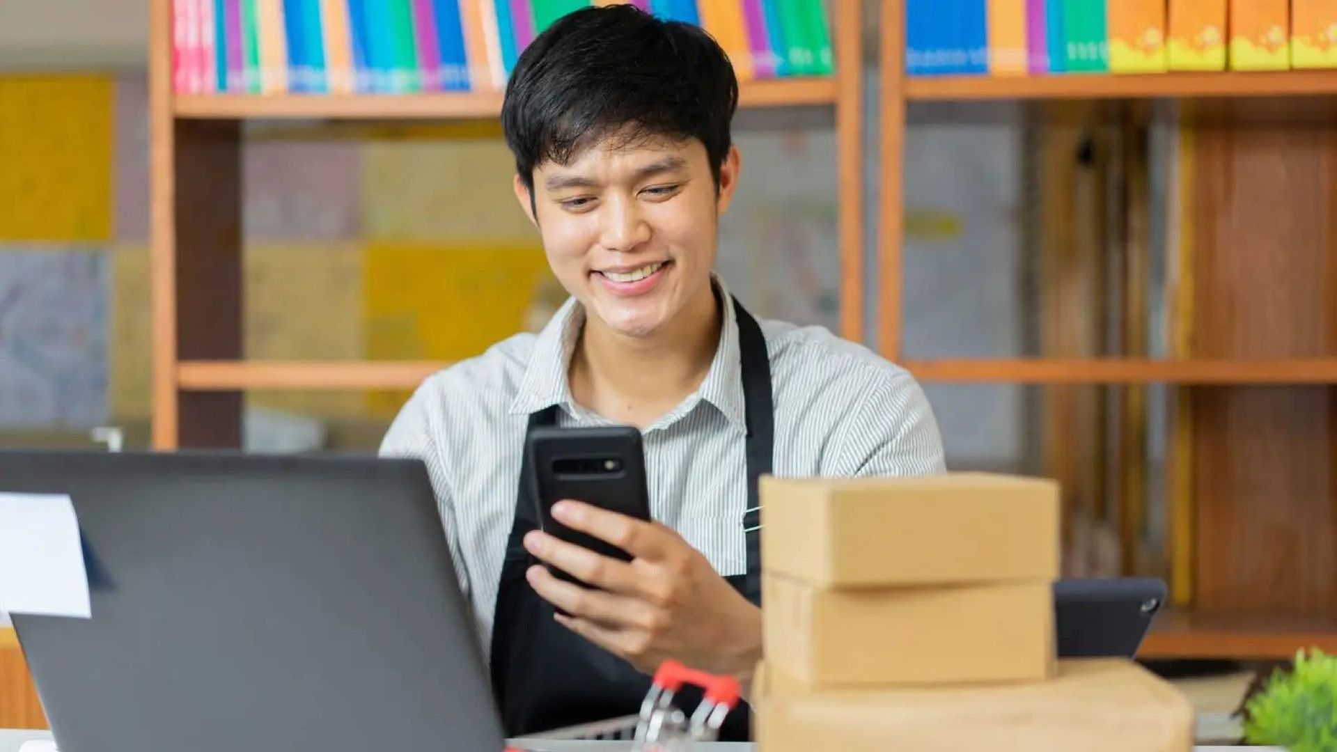 Young man with dark short hair and wearing an apron looks at a mobile phone.