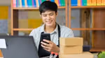 Young man with dark short hair and wearing an apron looks at a mobile phone.
