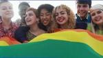 Young diverse people having fun holding LGBT rainbow flag outside